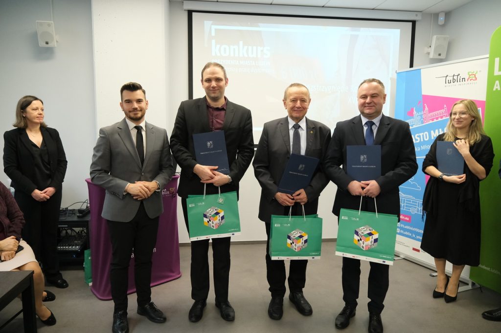 Czterech mężczyzn pozuje do zdjęcia. są uśmiechnięci, w rękach trzymają dyplomy i prezenty.