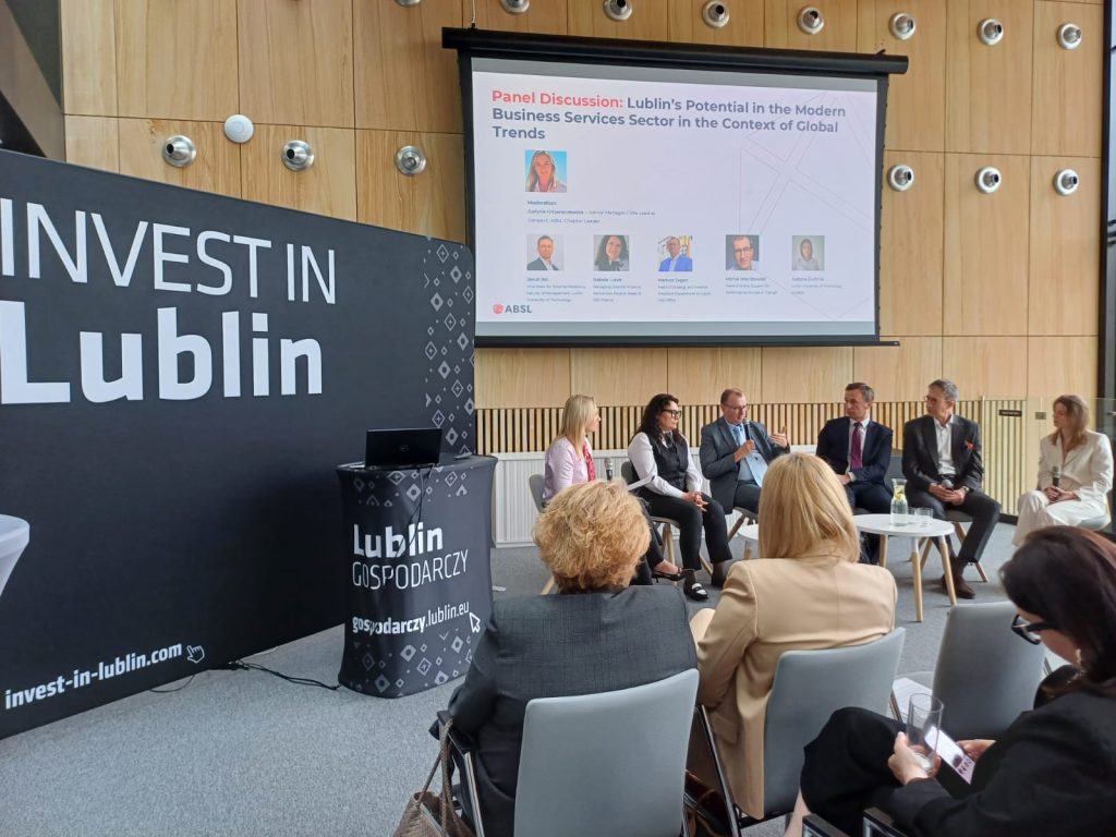 Sala konferencyjna pełna ludzi. Na pierwszym planie uczestnicy panelu dyskusyjnego. 