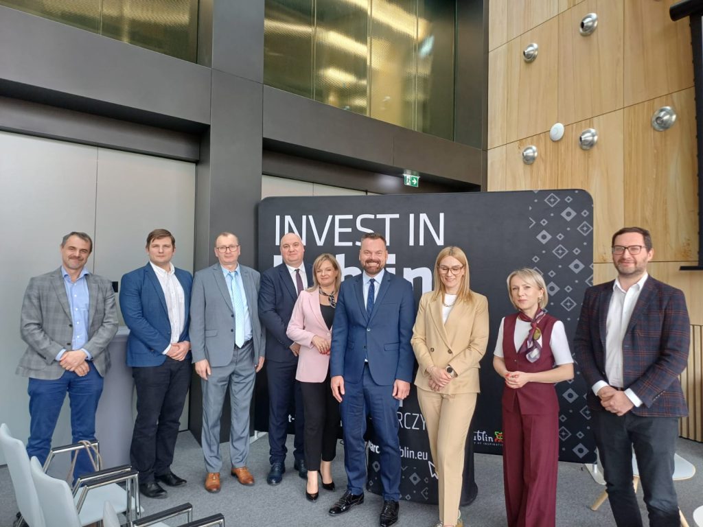 Grupa przedstawicieli biznesu, nauki i administracji publicznej na ściance promocyjnej - Invest in Lublin. 